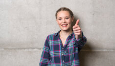 Lächelnde Studentin vor Wand mit "Daumen hoch"